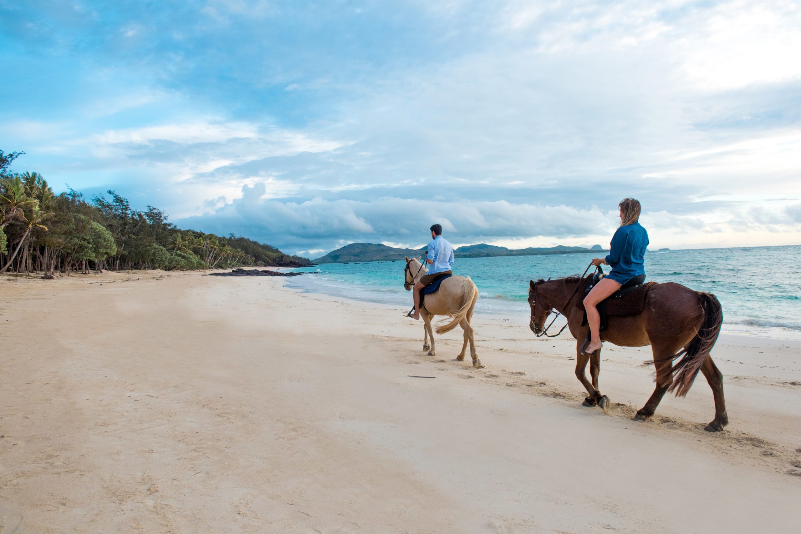 Couple enjoying horseback riding along a tropical beach in Fiji with turquoise waters
